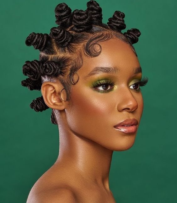 Mulher negra posa com um penteado para cabelos crespos, conhecido com bantu knots e baby hairs, em um fundo verde usando maquiagem com a mesma cor.