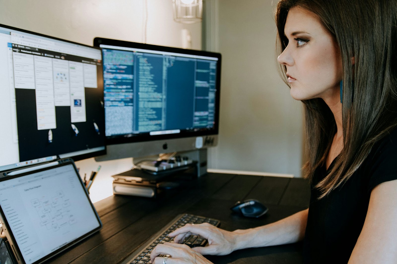 A woman working at her desk with two monitors displaying code and other work-related applications.