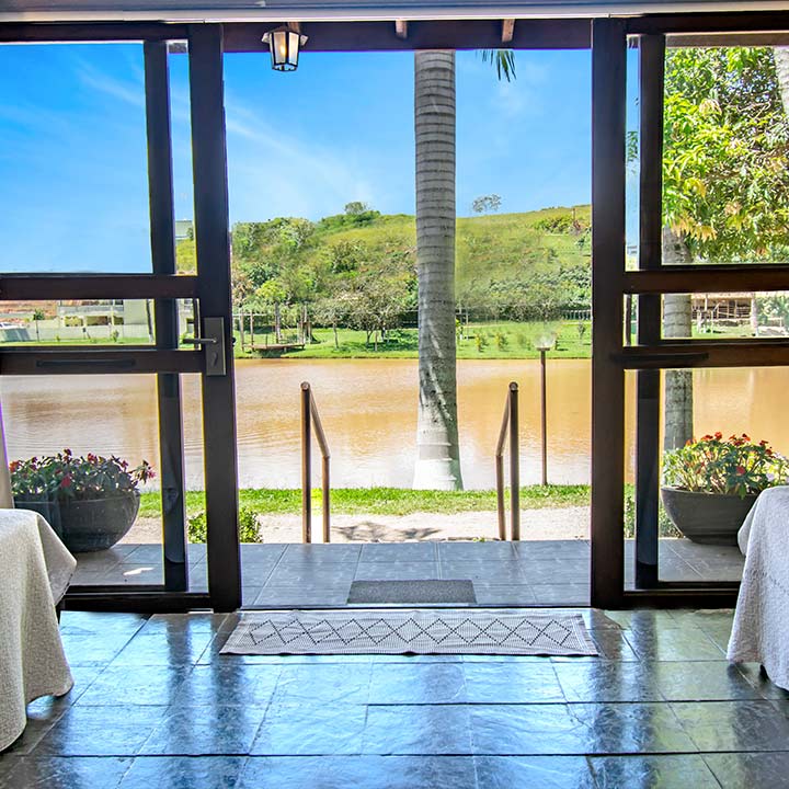 Vista encantadora de um ambiente interno com saída para um lindo lago e natureza exuberante ao fundo, ideal para relaxamento e eventos.