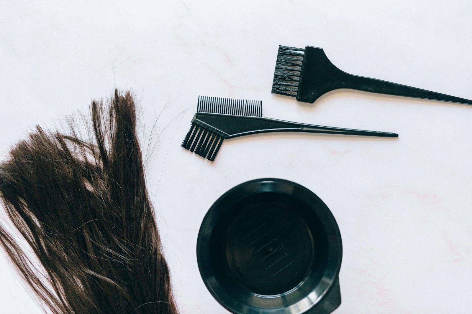 A black bowl accompanied by a brush and a comb, symbolizing the use of herbal hair dye over chemical alternatives.