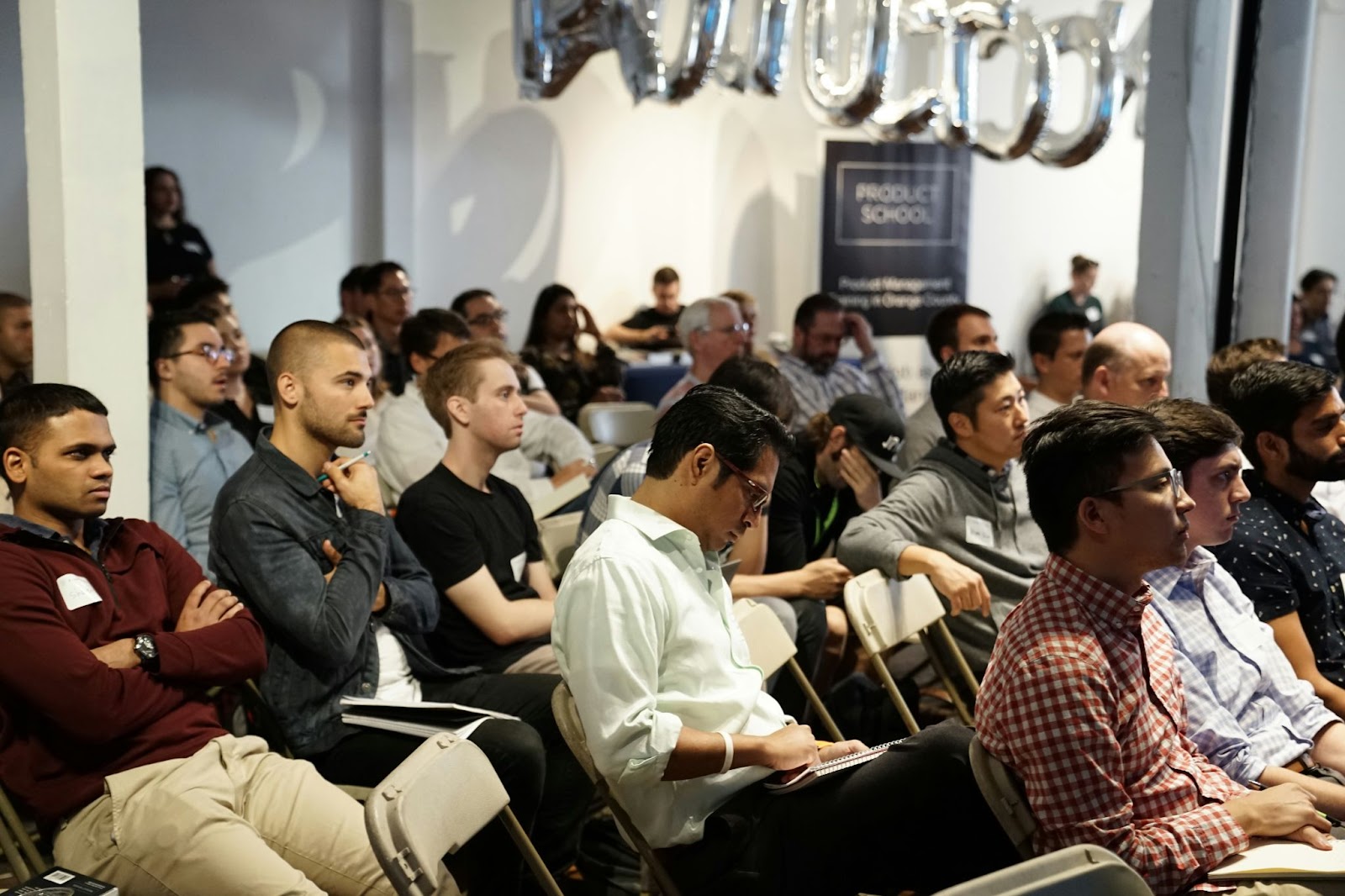 A group of people seated in rows, attentively listening to a presentation in a conference room.