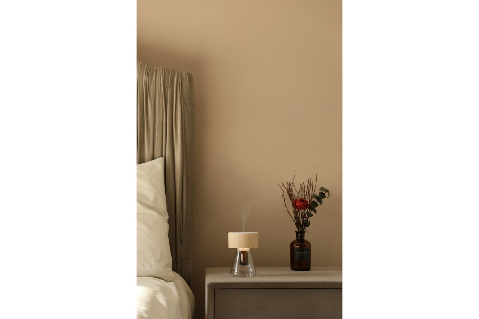 A reed diffuser bottle with flowers on a bedside table.