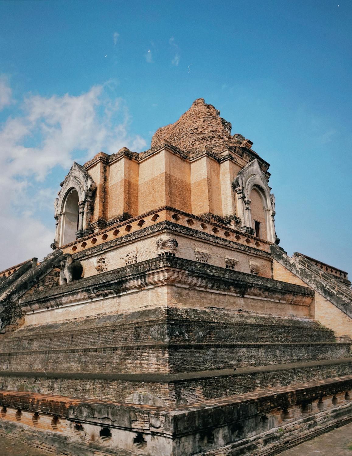 A stone building with a stone structure with Wat Chedi Luang in the background

Description automatically generated with medium confidence