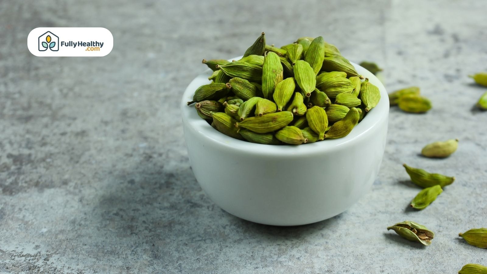 White ceramic bowl filled with green cardamom pods on stone