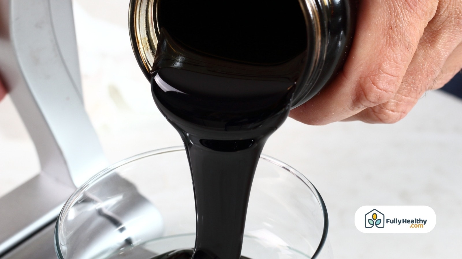Thick blackstrap molasses pouring from jar into glass container