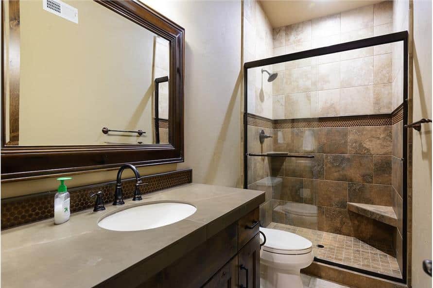 This bathroom is equipped with a wooden vanity, a toilet, and a walk-in shower complete with a corner seat and wrought iron fixtures.