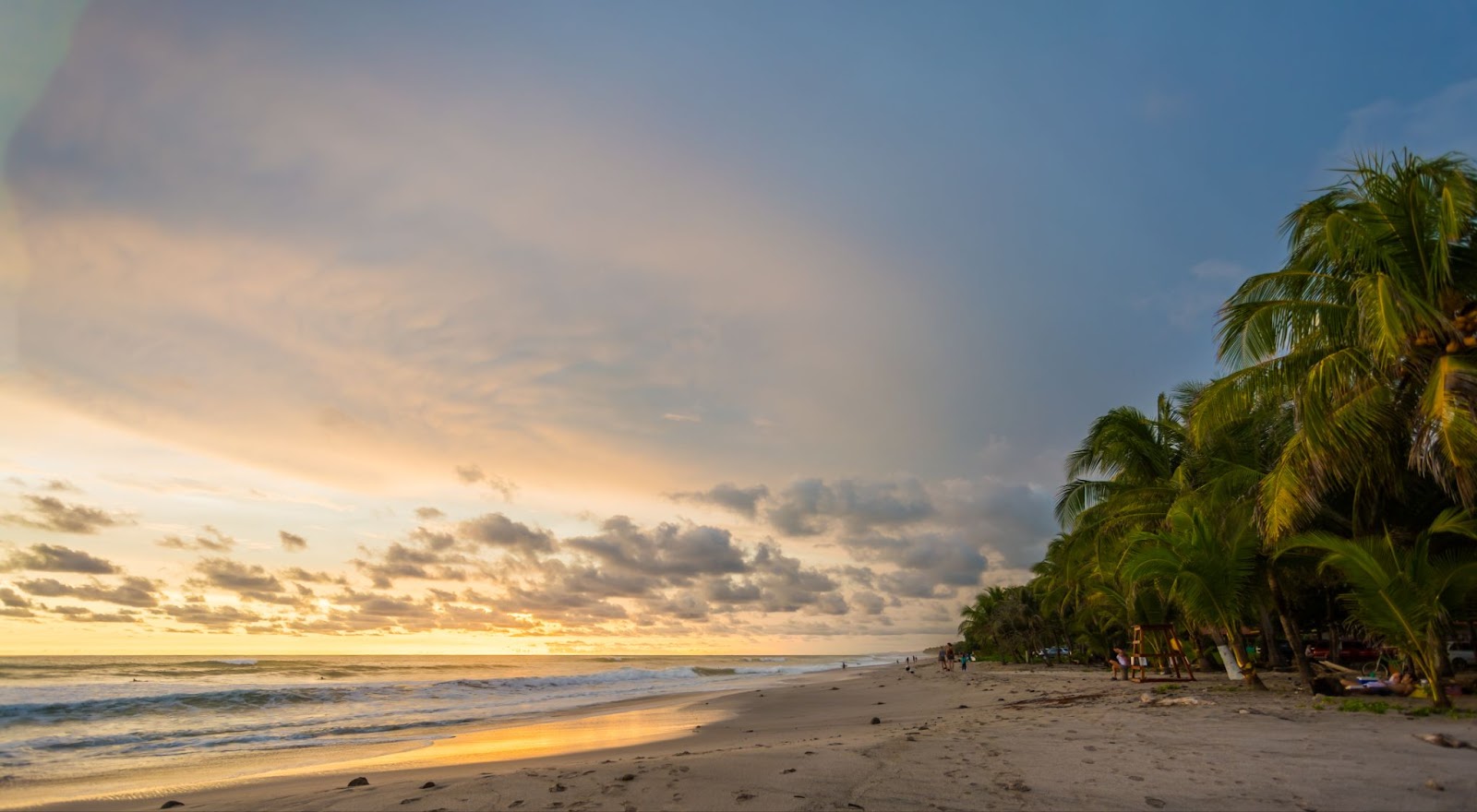 Sunset at Santa Teresa Beach, Costa Rica, with surfers in the waves, golden skies, and palm-lined shores, capturing the essence of surf culture and upscale travel.