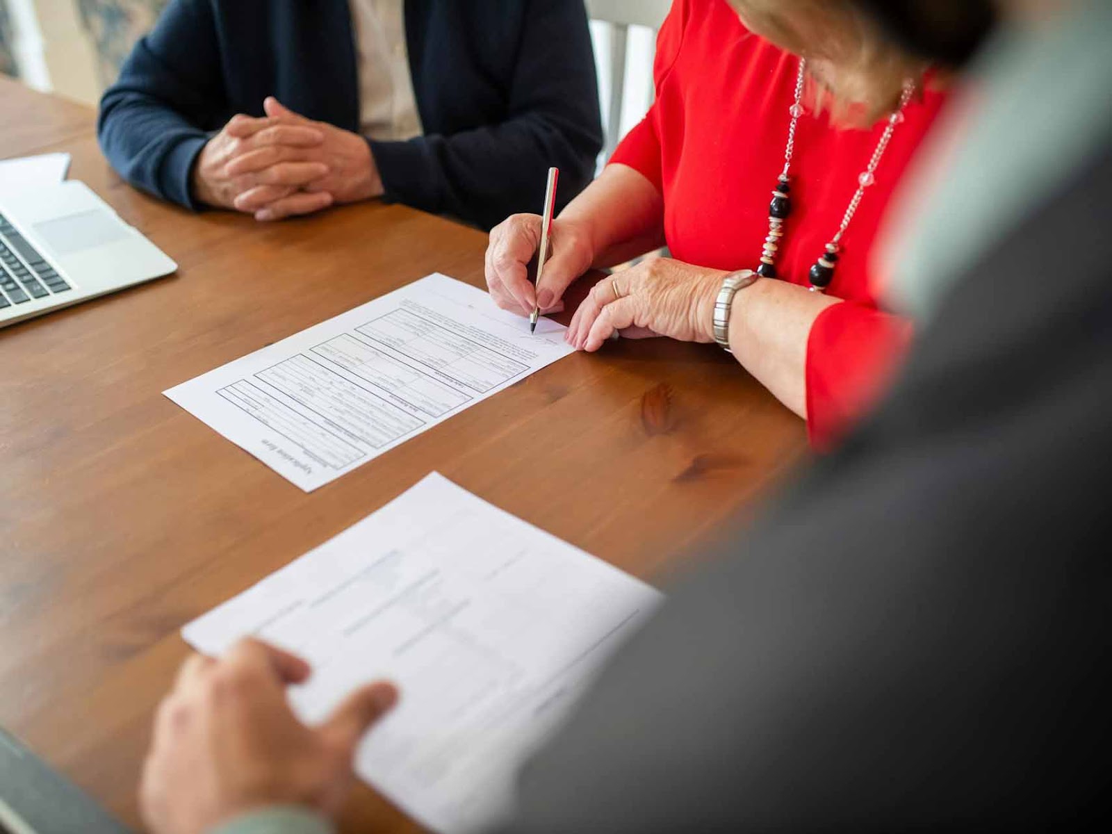 Two people sitting at a wooden table with paperwork and a laptop, one person signing documents, illustrating the process of applying for short-term disability approval for anxiety and depression.