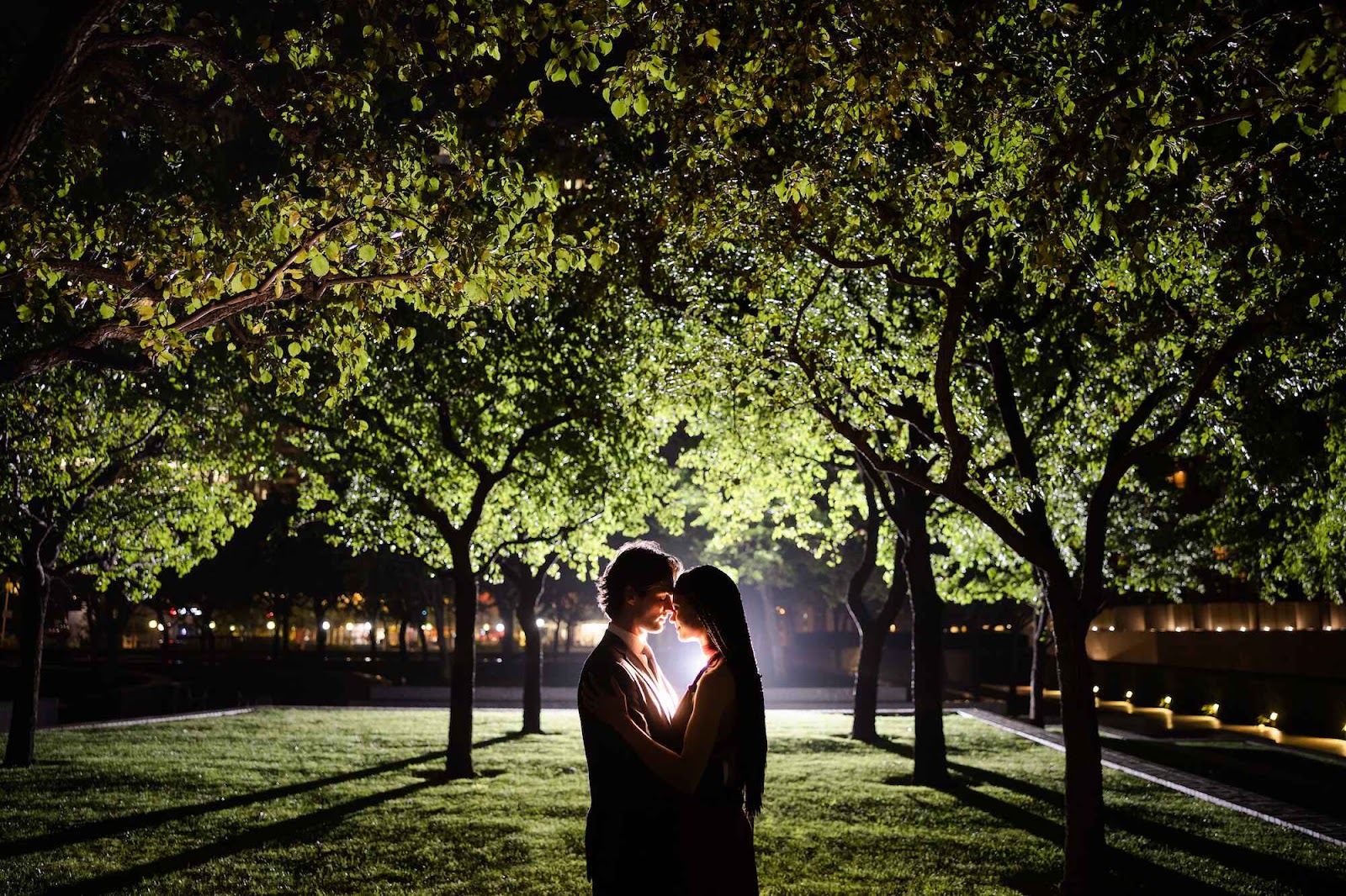 Enchanting night-time wedding photo of a couple in a garden, hugged by the glow of dim lighting.