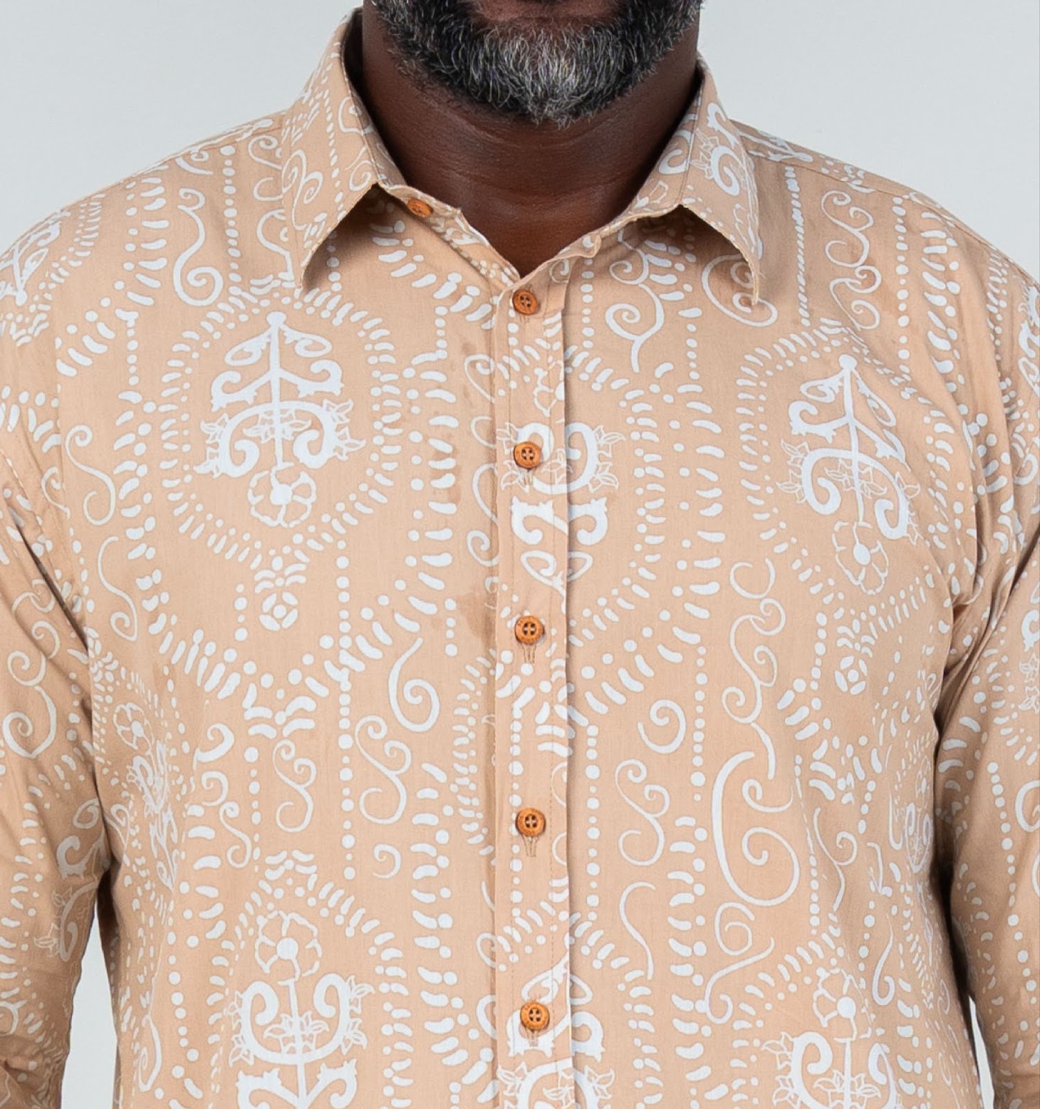 A closeup image showing long sleeved men's batik shirt in tan petola from batik boutique, standing in a office