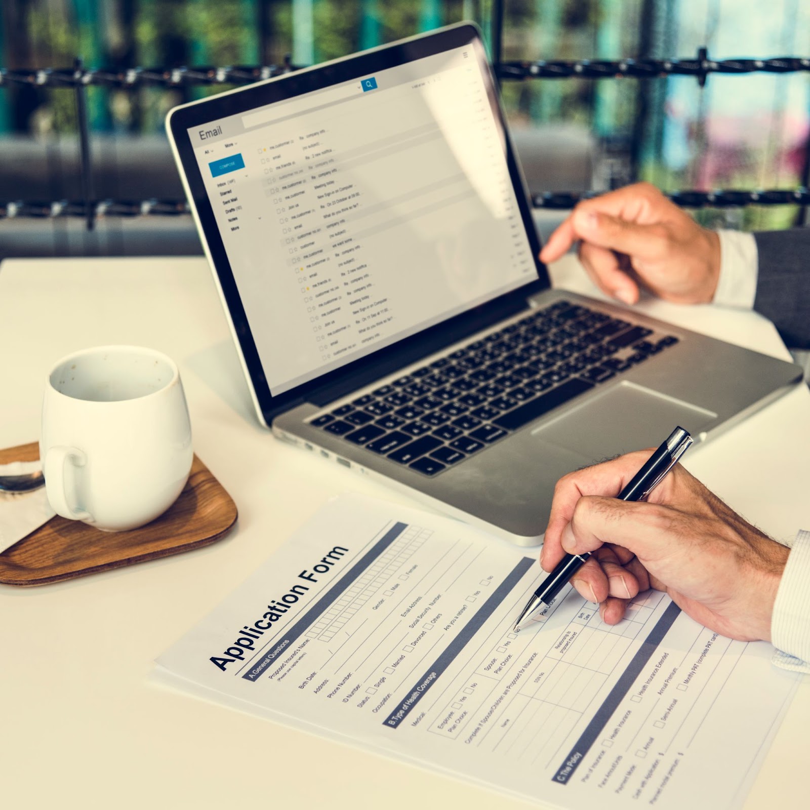 Man with a pen filling out an application form next to a cup of coffee and a laptop. 