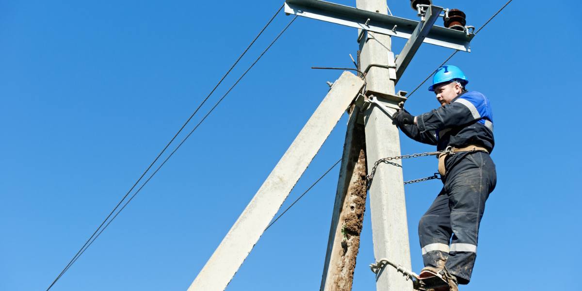 Journeyman Electrician performing maintenance on an overhead power line while securely harnessed to a utility pole.