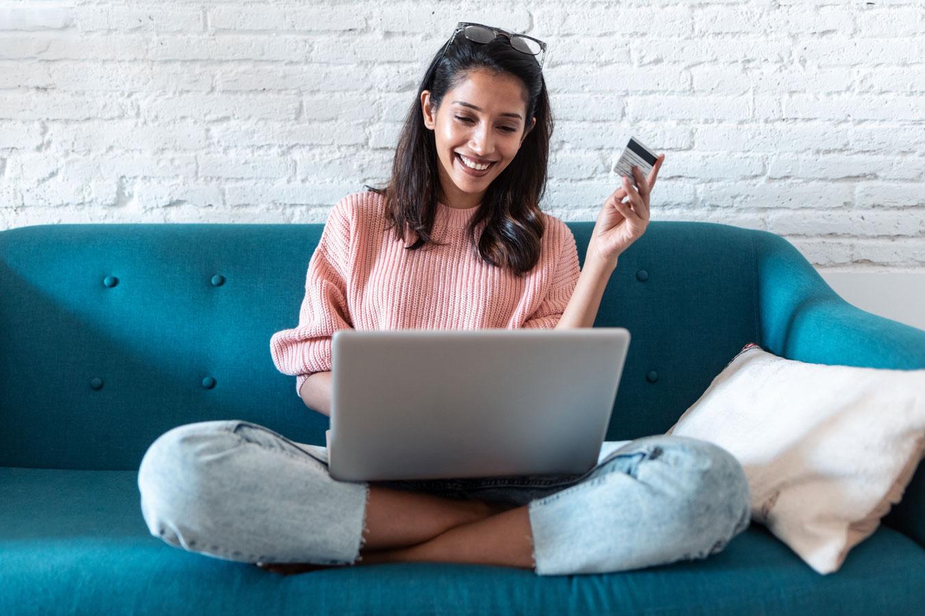 South Indian female in pink jumper on sofa with laptop and credit card