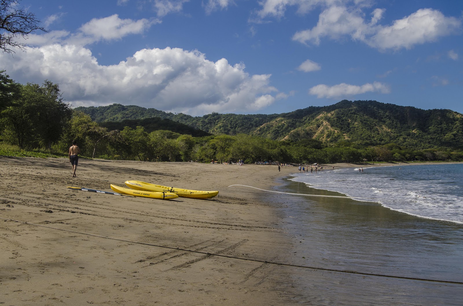 A beach with clear water, mountains in the distance, and a kayak resting on the land.