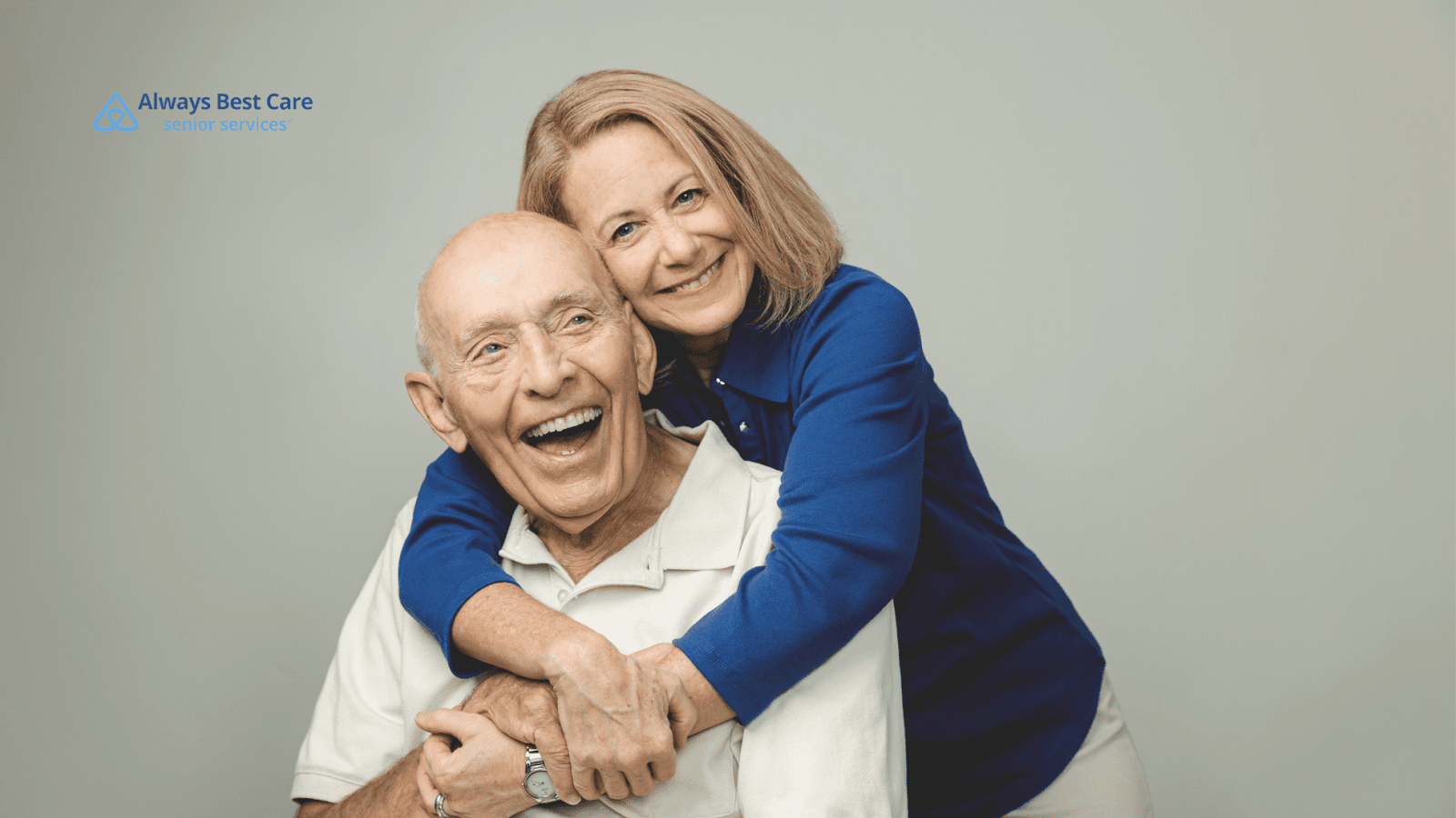 This image depicts a senior man smiling while being hugged by a family member