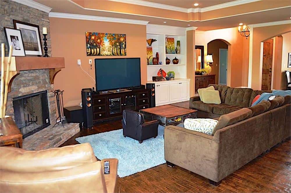 Family room with a stone fireplace, a TV, an L-shaped sectional, leather armchairs, and a white built-in cabinet.