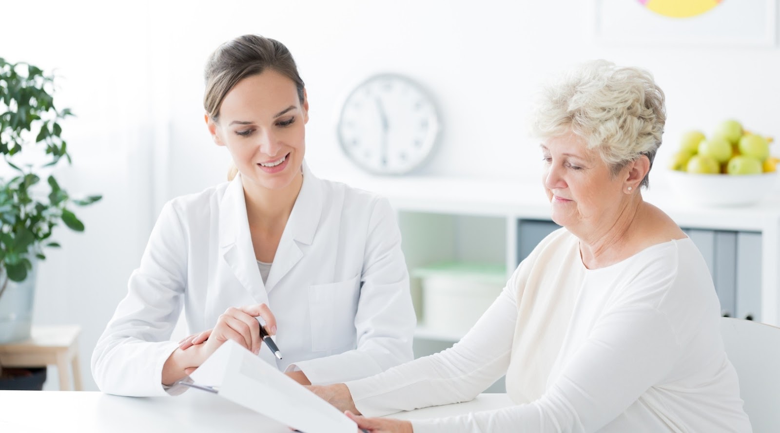 Dietitian smiling while explaining a document to an elderly woman in a bright nutritionist office.