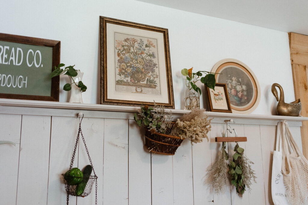 Pictures sitting on a shelf and dried flowers hanging from pegs. 