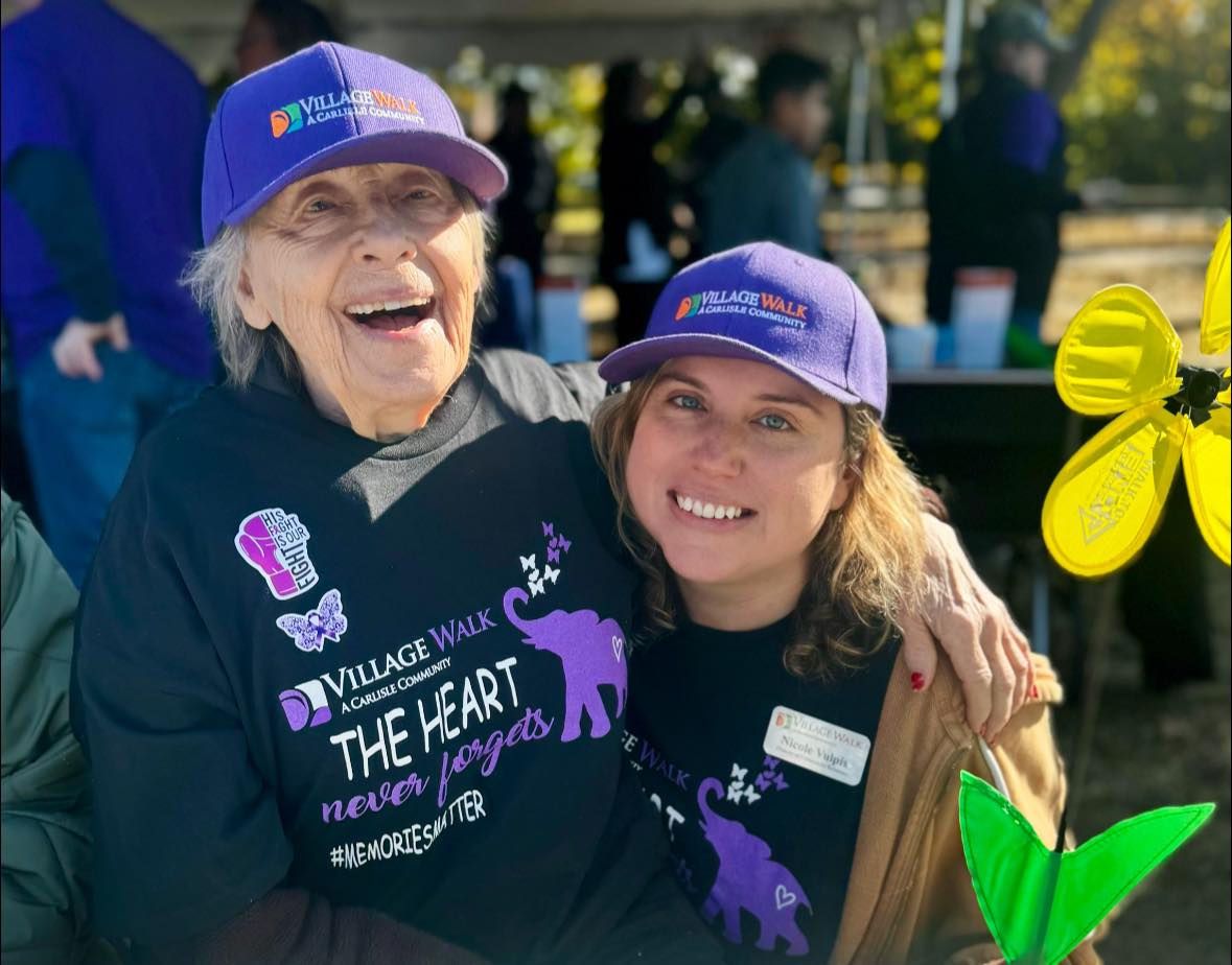 A Village Walk staff member smiling with an elderly person next to them