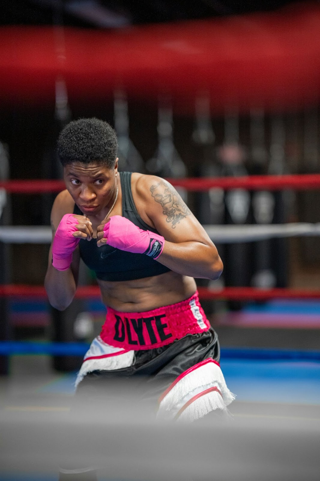 A woman in red and white jersey shirt and white shorts in a boxing ring.