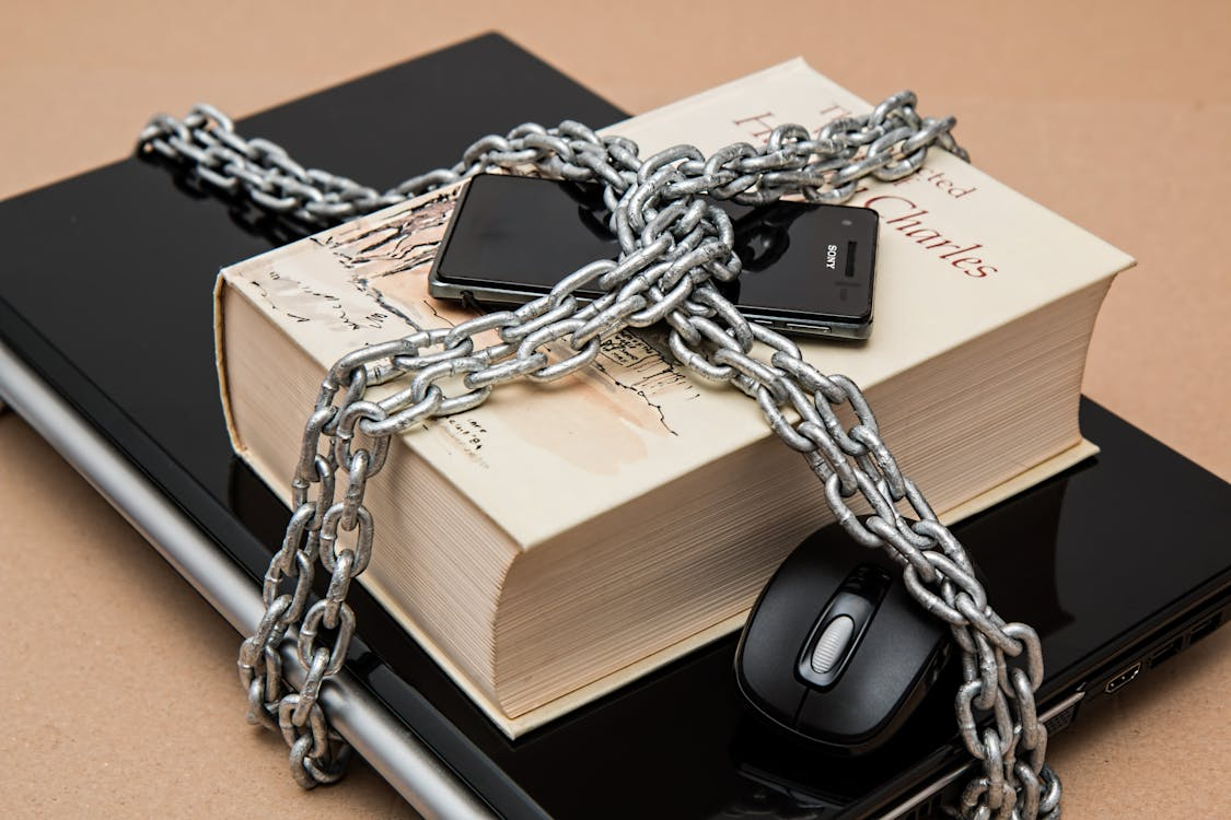 Book, phone, and laptop secured with chains, symbolizing information protection.