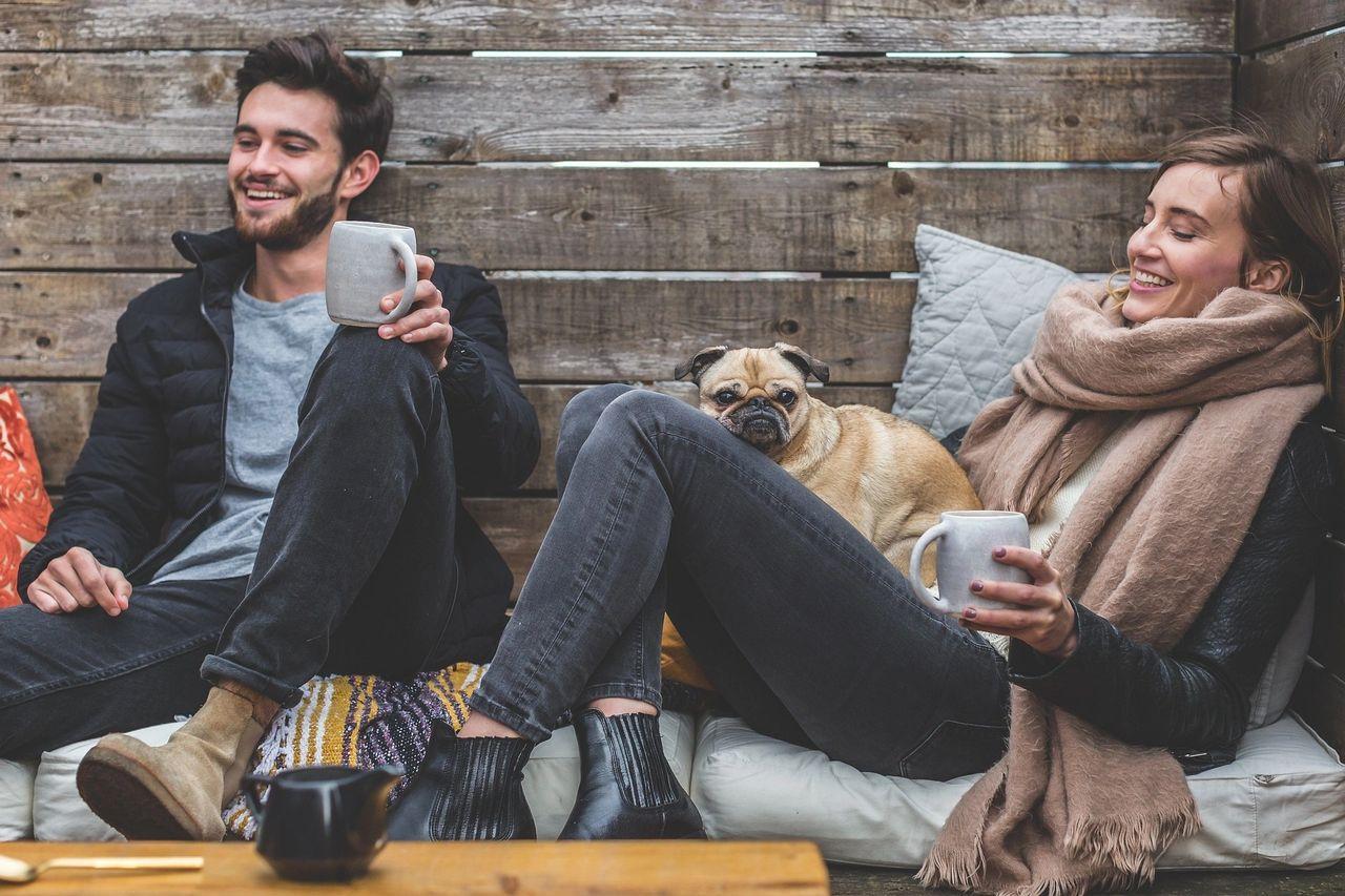 couple sat drinking coffee with their small pug cross dog 