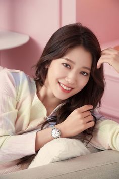 This contains a picture of Shin Hye n sitting on top of a couch next to a pink wall 