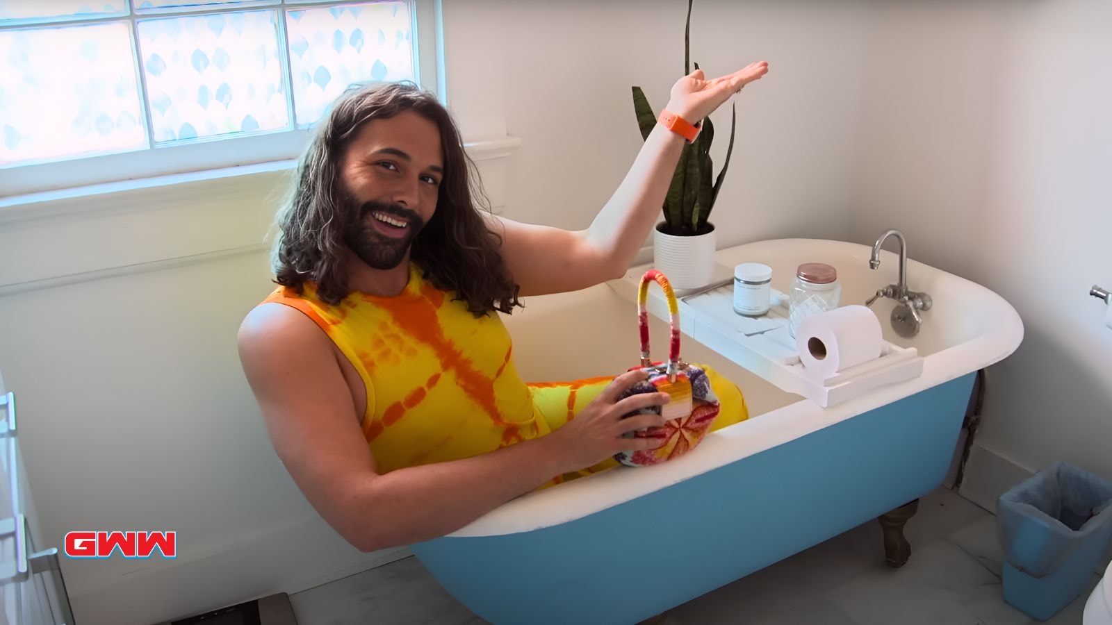 Jonathan Van Ness humorously sitting in a bathtub, smiling brightly.