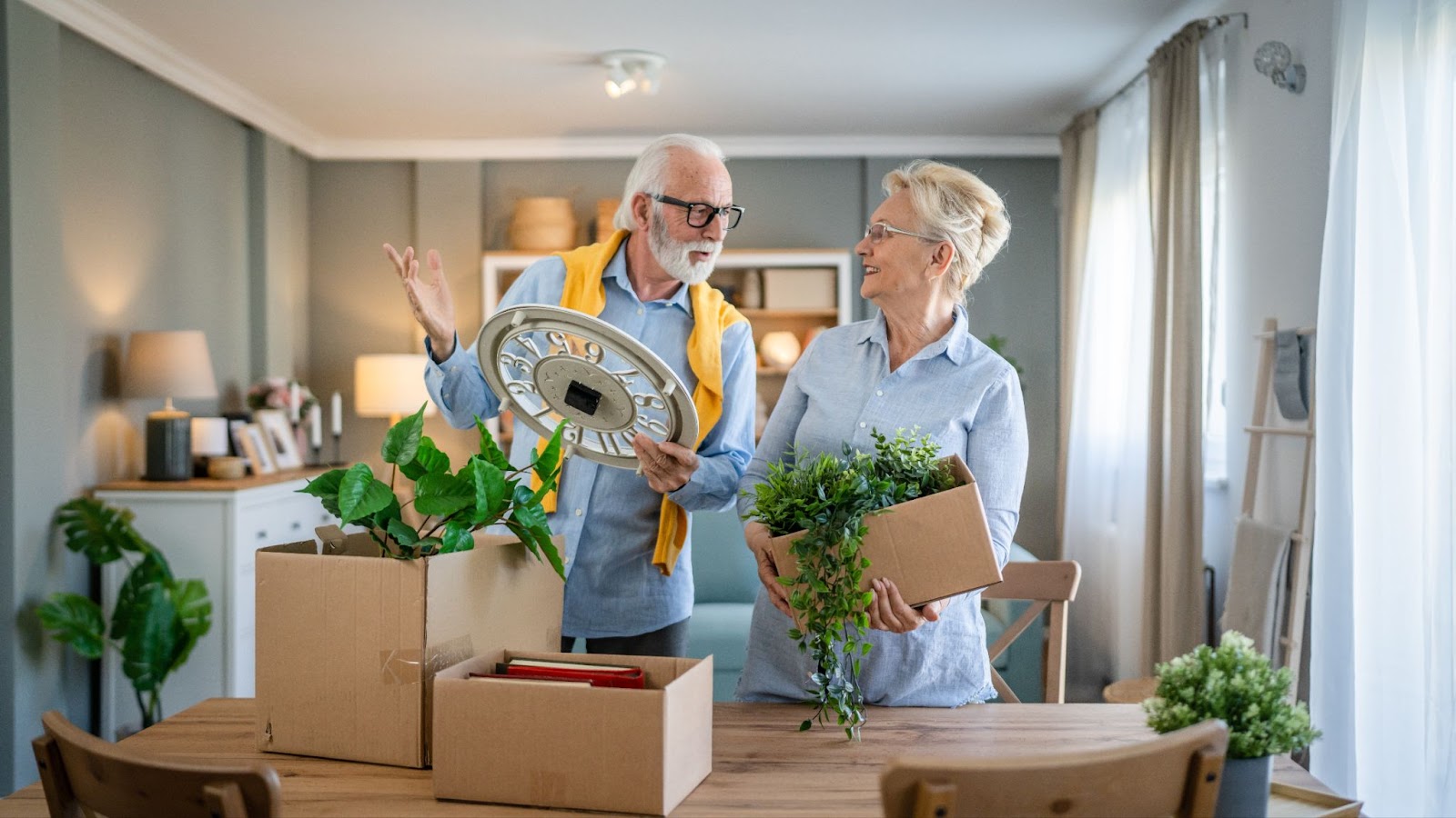 An older adult couple unpacks boxes of their belongings and discusses where to arrange them in their new assisted living home