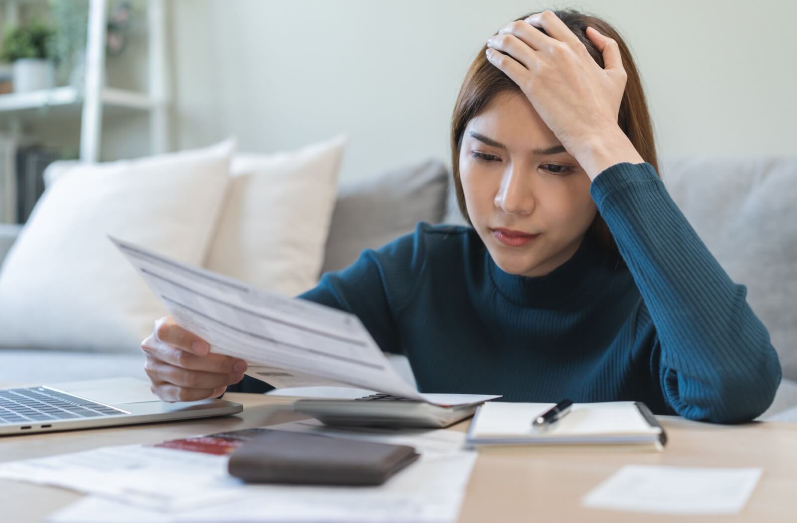 A stressed person cradles their head as they review a stack of bills.