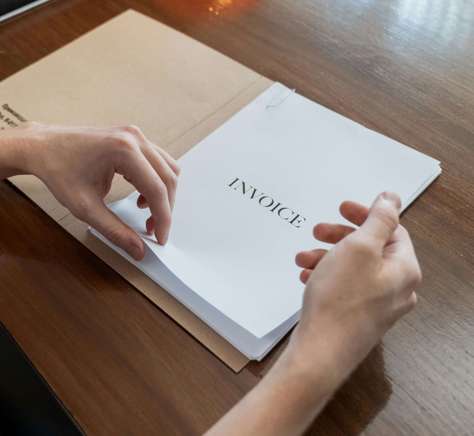 Hands holding a page with the word “Invoice” written on it.