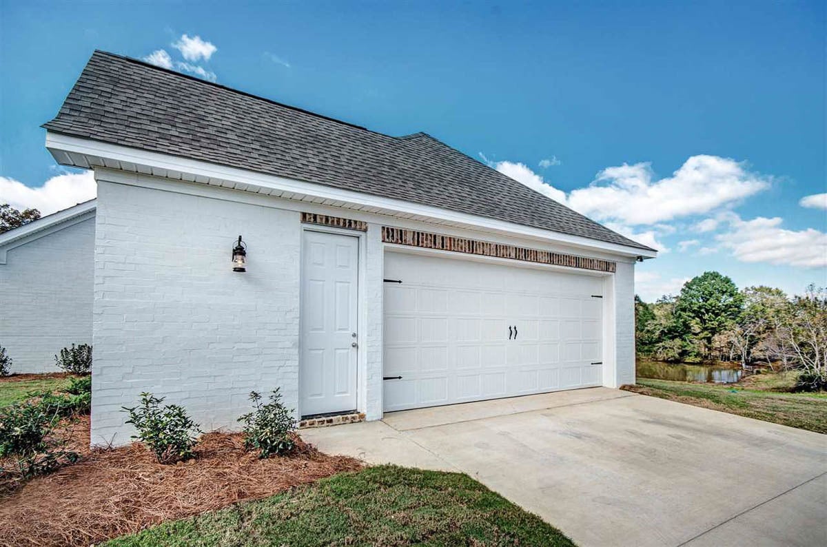 Side-entry garage with brick exterior, tiled roof, white garage door, and a man door leading to its storage room.