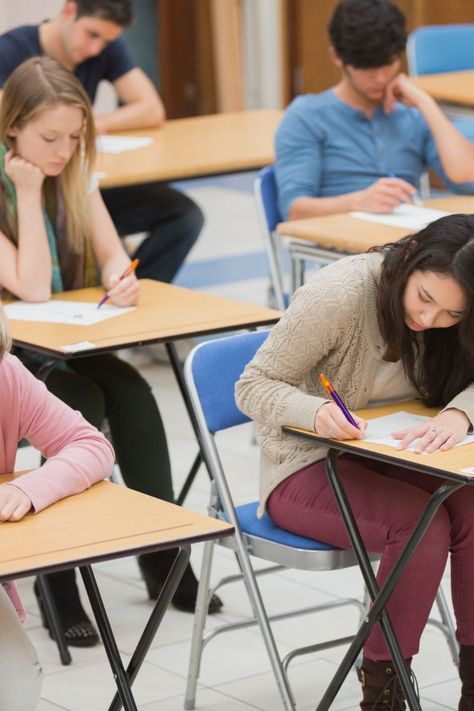 This contain several students sitting at desks in a classroom  writing 