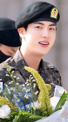 This contains an image of BTS Jin ona military uniform holding a flower  