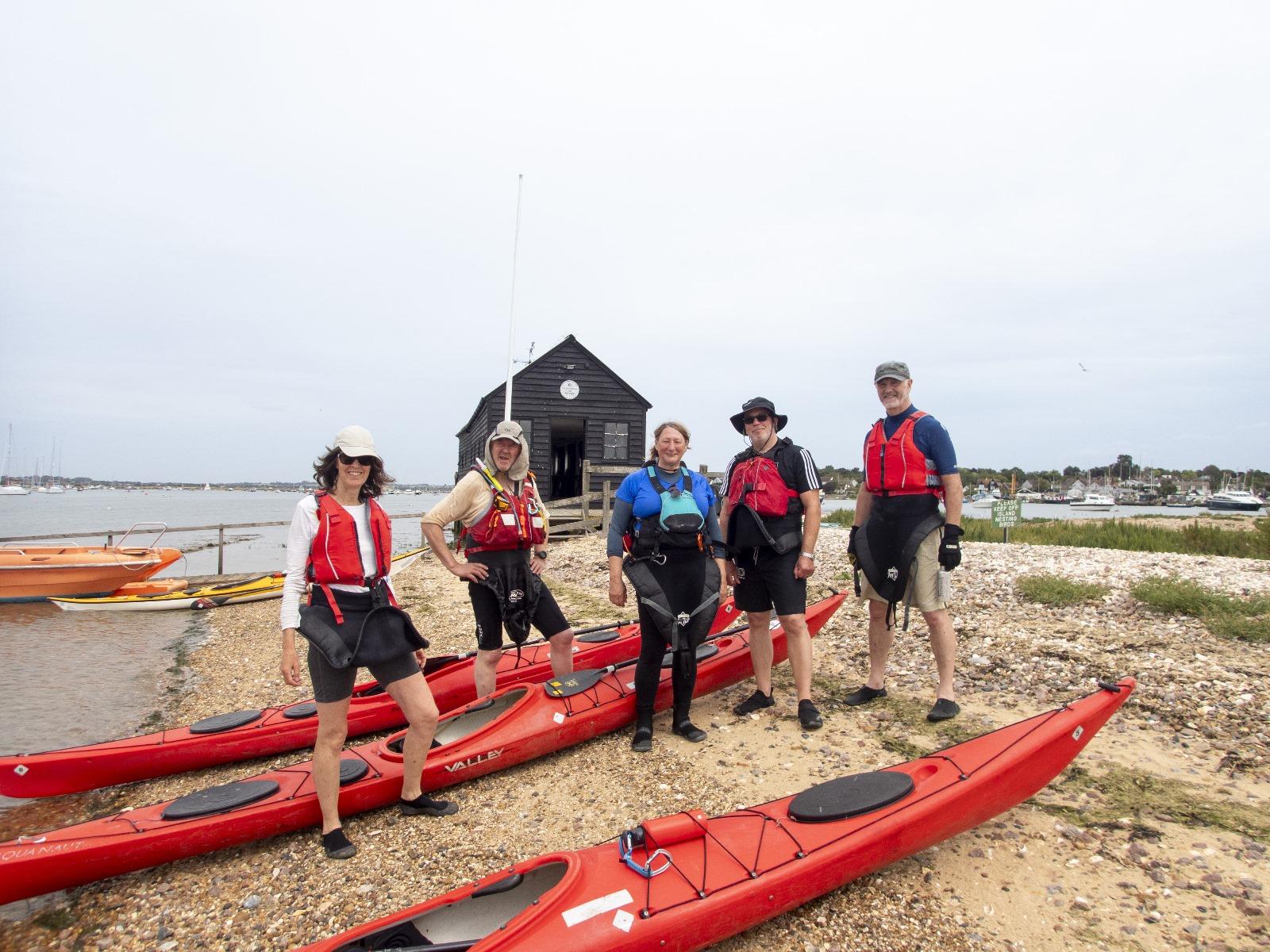 A group of people standing next to kayaks

Description automatically generated