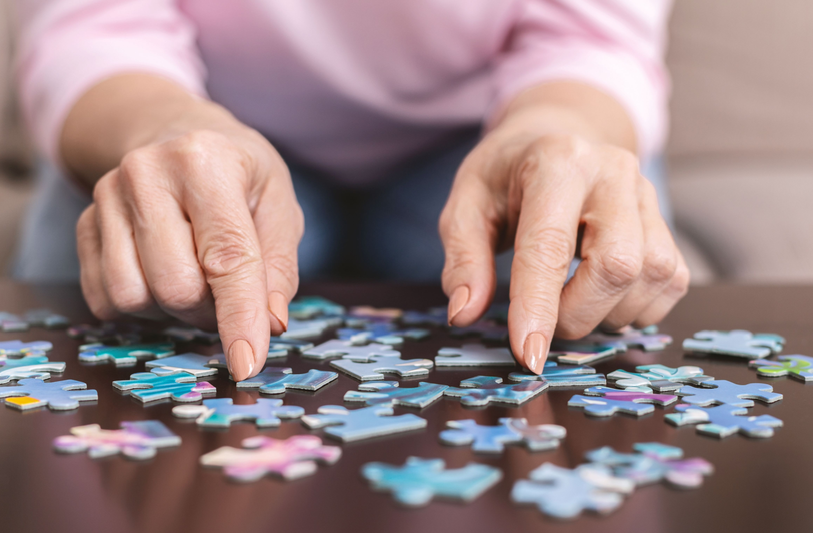 A senior with polished nails spreads puzzle pieces out on a coffee table.