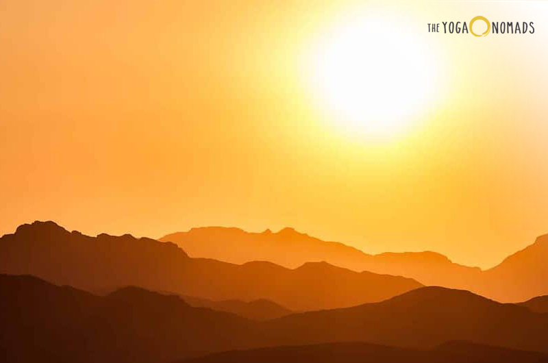 is yin good or bad? The image captures a stunning sunset behind mountain ranges, with warm hues of yellow and orange creating a silhouette effect on the mountains. The sky is clear, adding to the serene and tranquil atmosphere.