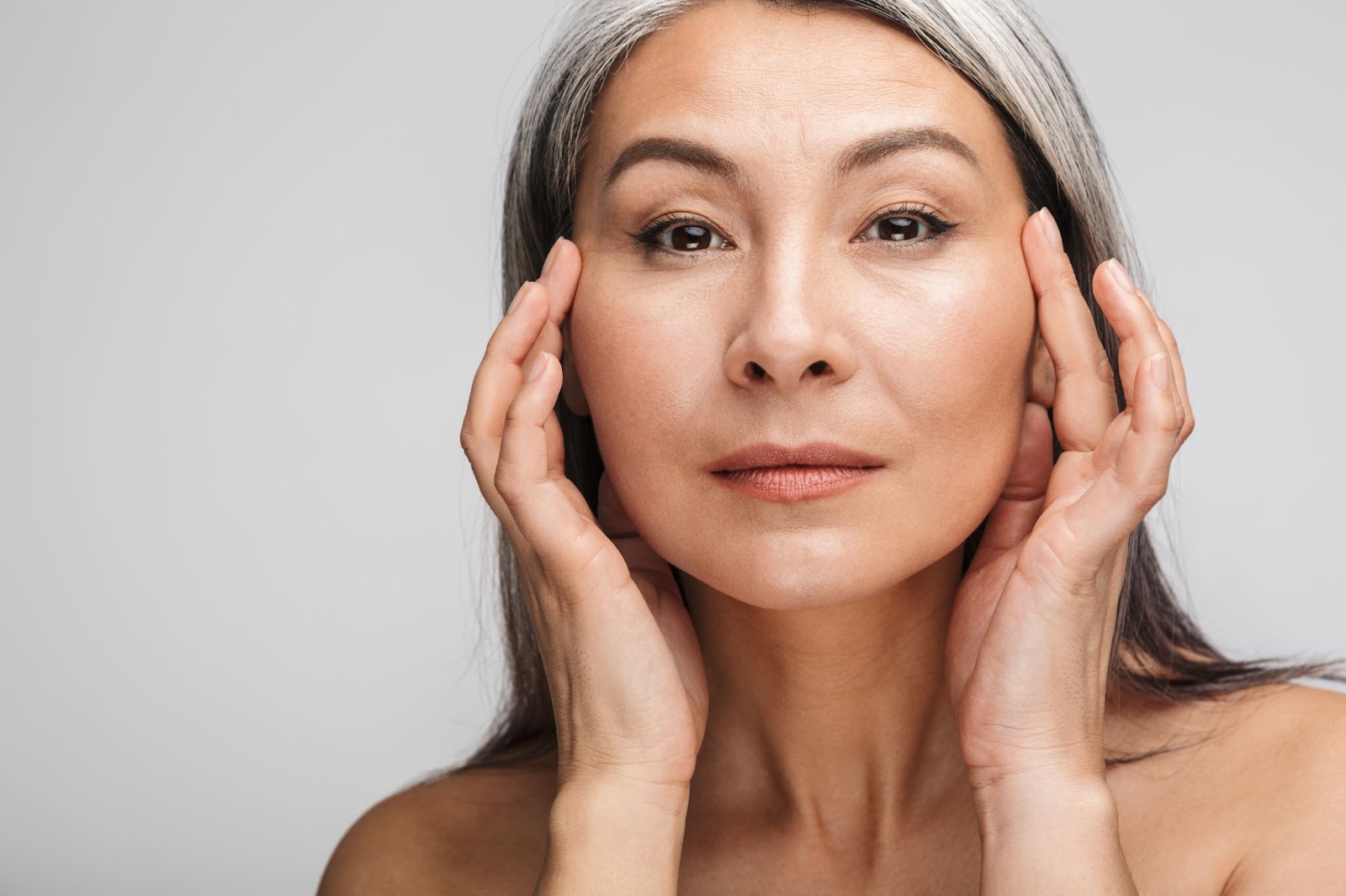 Close-up of an attractive older woman as she holds her hands on the sides of her face.