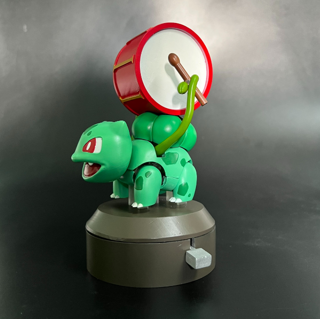 3D printed Pokémon Bulbasaur automata with a red drum on its back, featuring flexible, articulated parts.