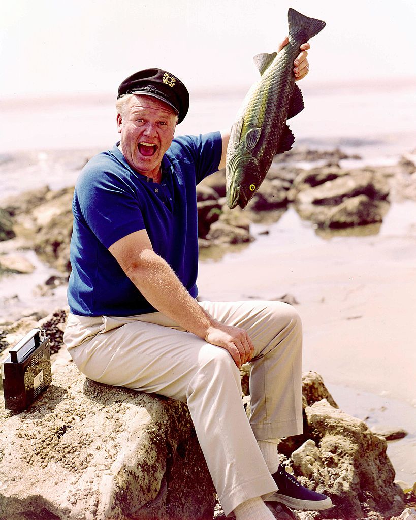 Alan Hale Jr assis sur un rocher et tenant un poisson dans un portrait publicitaire pour la série télévisée "Gilligan's Island", dans laquelle Hale Jr jouait "The Skipper", États-Unis, vers 1967.