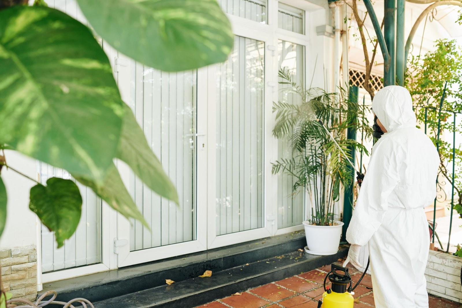 Professional pest control worker in protective gear conducting a treatment at the home’s entry.