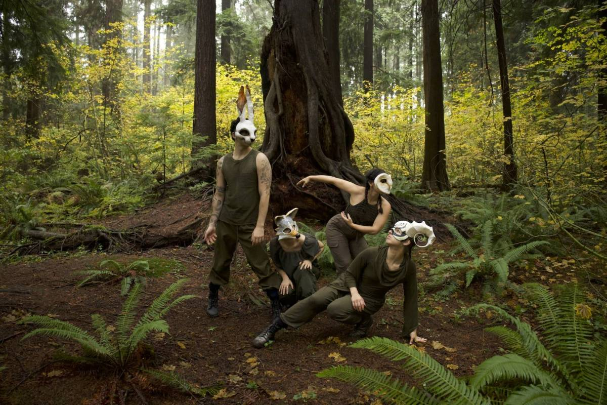 Four people wearing white animal masks pose in a forest