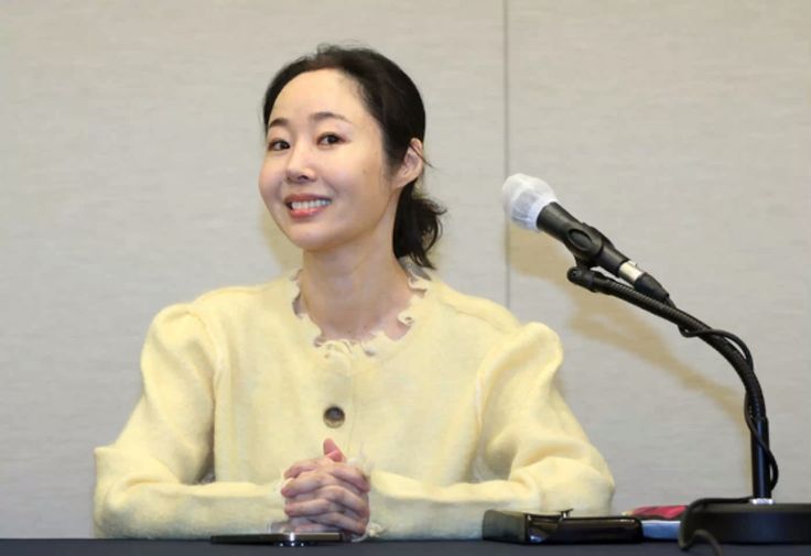 This  contain an image of CEO Min Hee Jin, sitting at a table in front of a microphone with her hands folded out