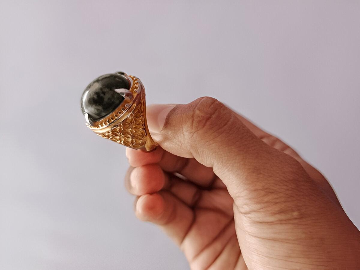 Close up view of adult man's hand holding agate ring with moss green pattern