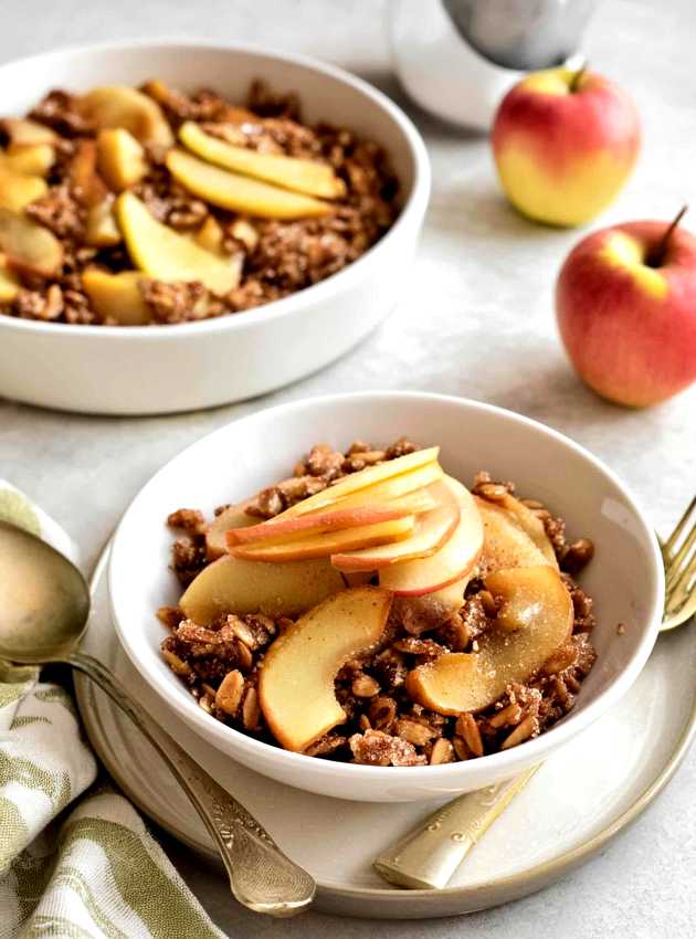 Apple crisp with baked apple slices and a crunchy oat topping served in white bowls.