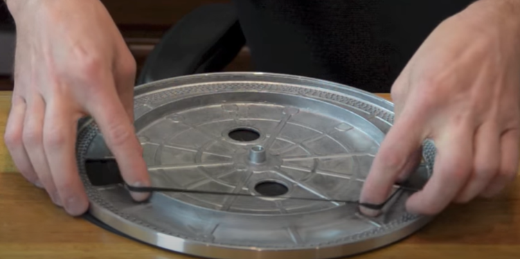 Hands installing a belt on the underside of a turntable platter.