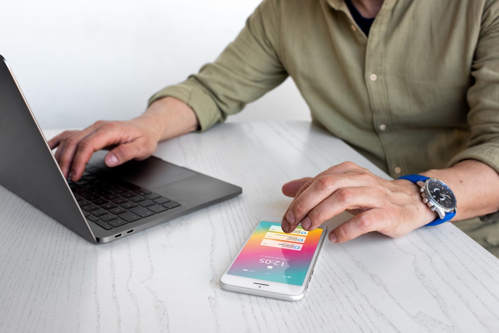 A man typing on his laptop while using his phone