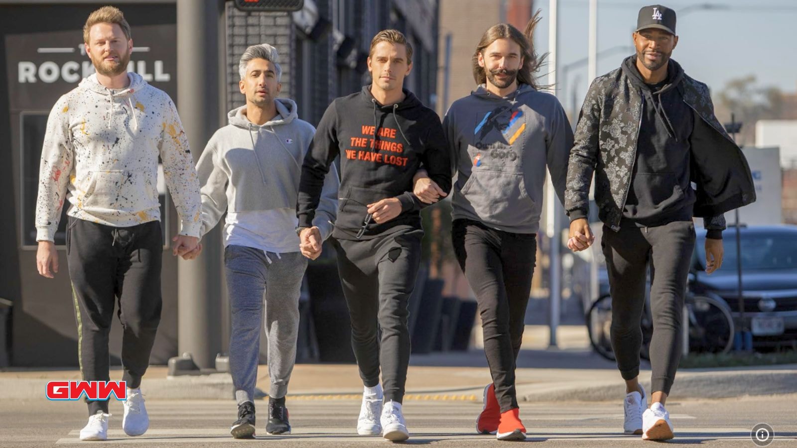 The Fab Five walking confidently down a city street, holding hands.