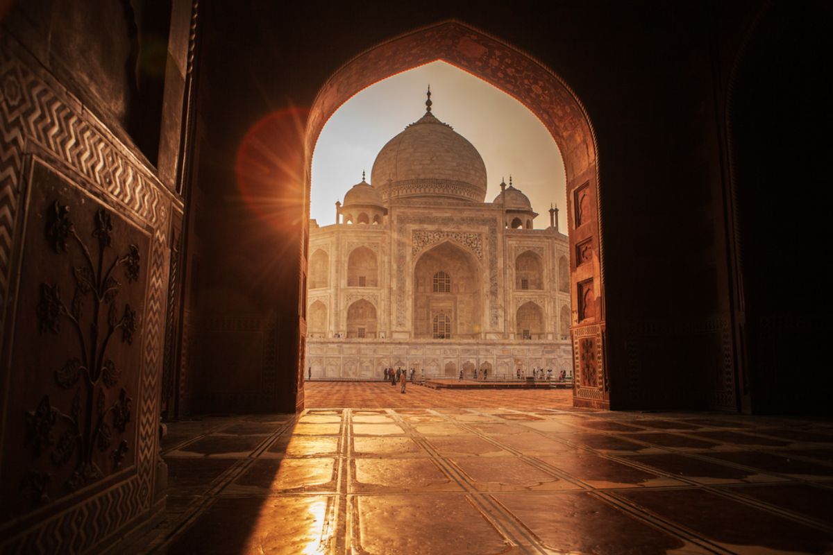 shows a view of the white marble mausoleum, the Taj Mahal, framed by a red sandstone archway.