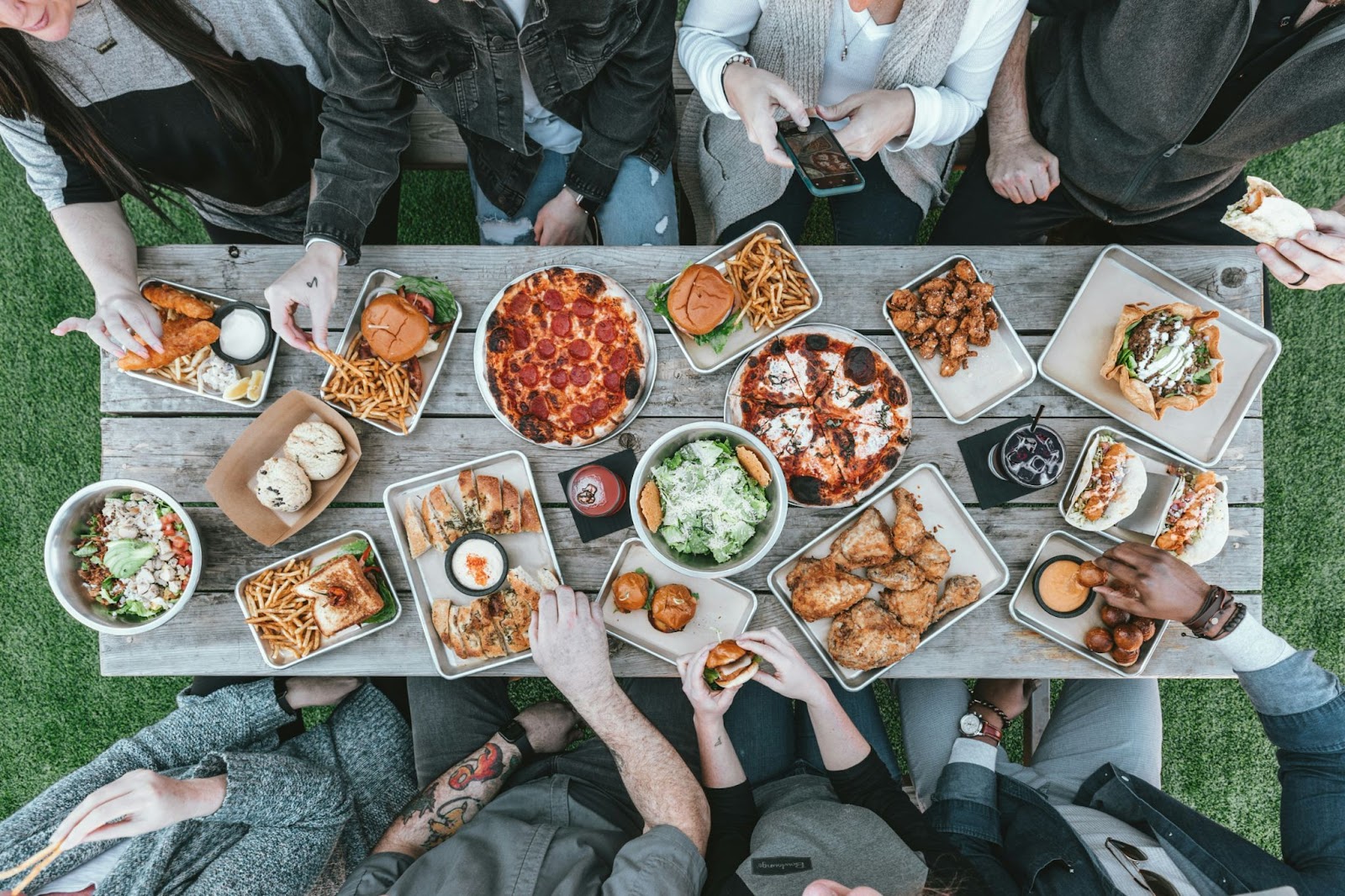 Overhead view of a picnic table covered with a wide variety of foods and people sharing a meal—illustrating food freedom, variety, and the inclusive nature of intuitive eating.